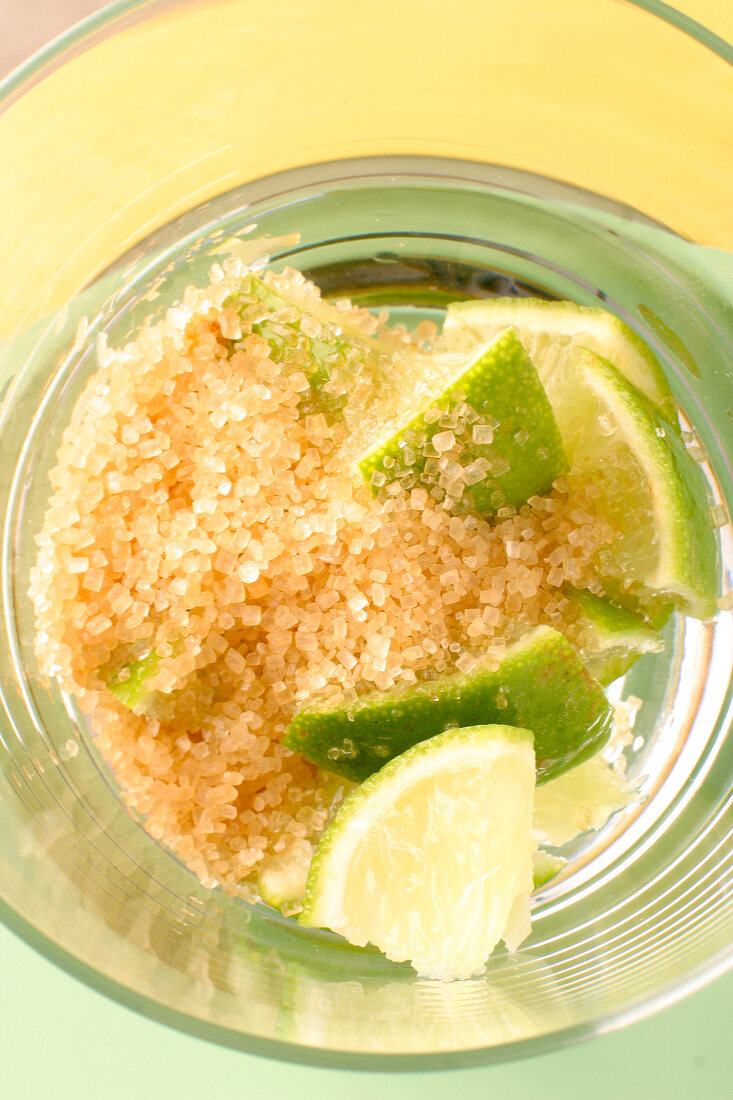 Brauner Zucker im Glas mit Limonenstücken für Caipirinha