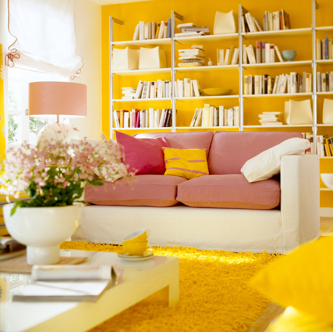 White couch with pink cushions and small table with flower vase in living room