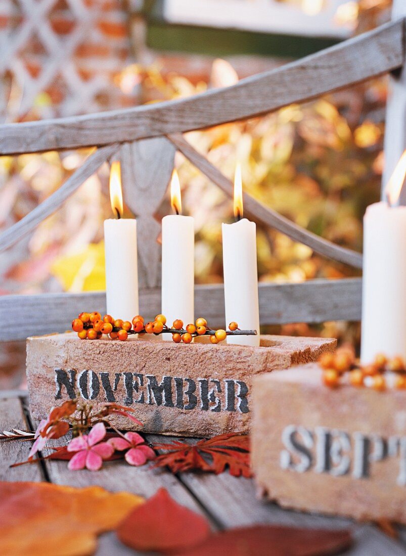 Candleholders made from bricks holding three white candles and decorated with leaves & berries