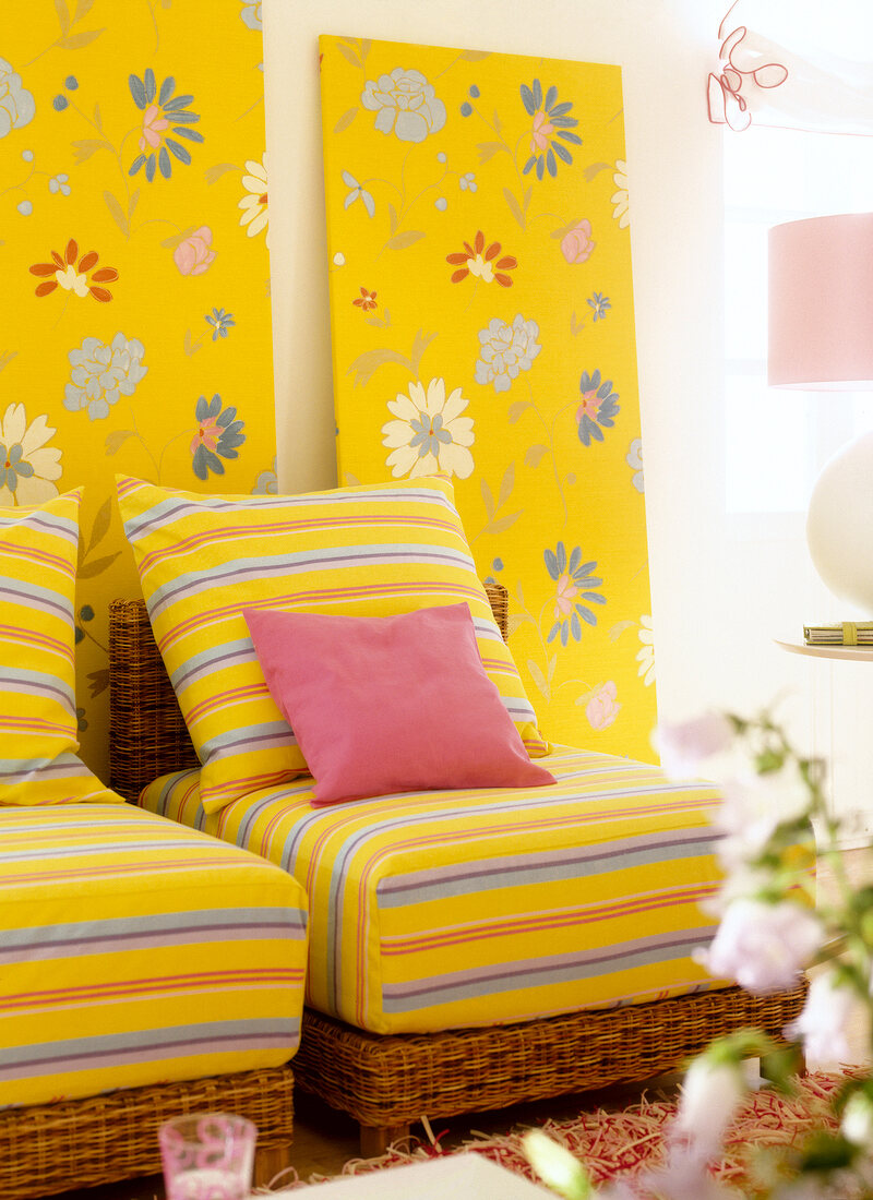 Yellow striped cushions on wicker chair against floral patterned wallpaper