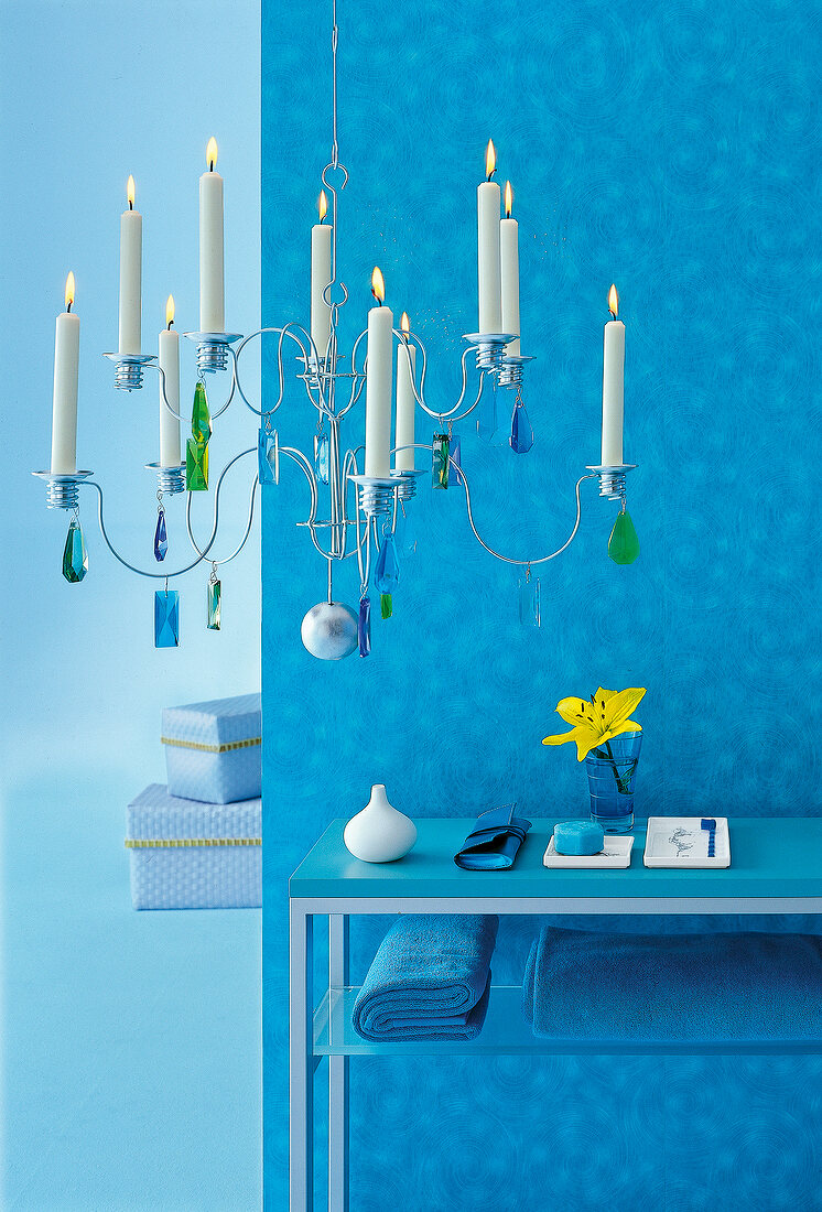 Lit candle on metal candlestick decorated with crystal stones against blue wall