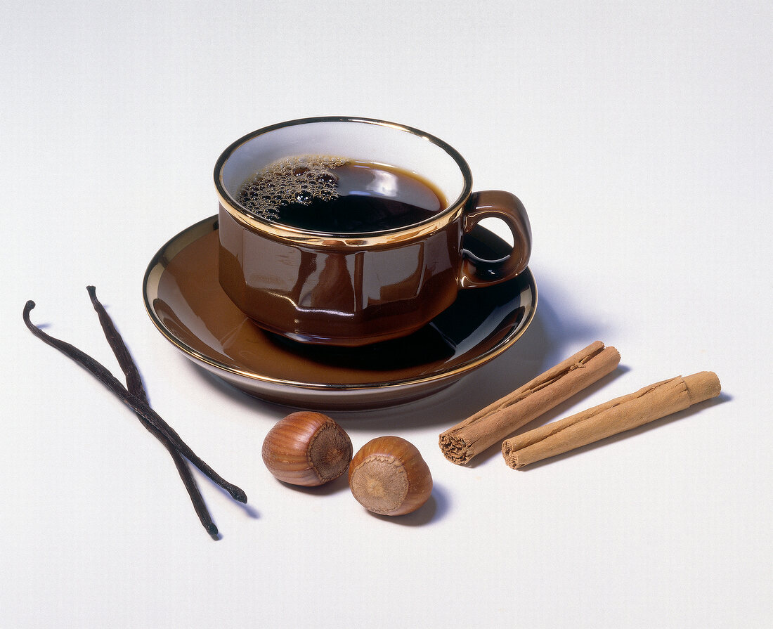 Cup of coffee with vanilla beans, hazelnuts and cinnamon on white background