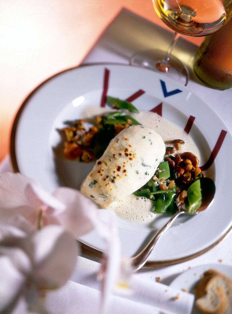 Soufflierter turbot in foamy sauce with beans and chanterelles on plate