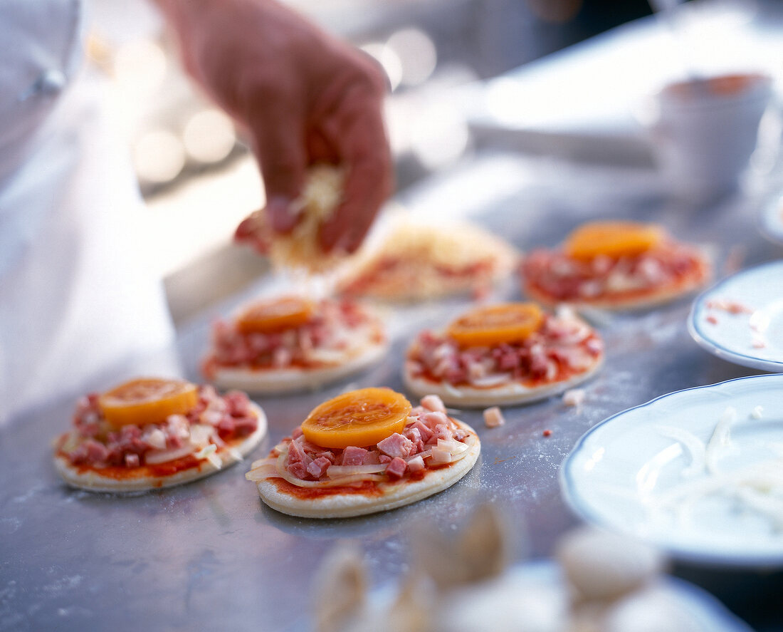 Pizza-Teigböden werden belegt mit Ferkelfleisch und Tomatenscheiben