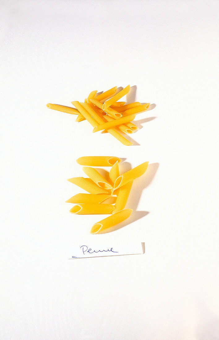 Raw penne pasta on white background