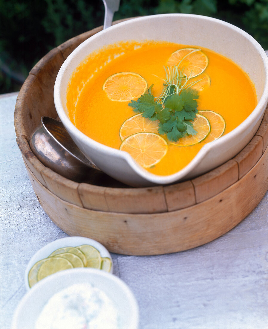 Carrot and coriander soup with lemon slices and coriander leaves in bowl