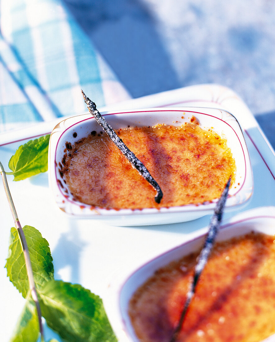 Creme brulee with vanilla sticks and mint leaves in baking dish