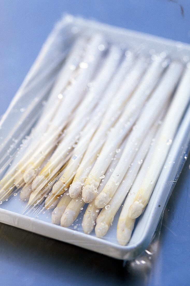 White asparagus spears in a tray covered with food wrap