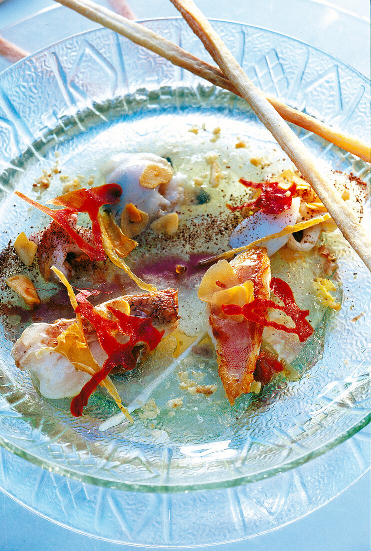 Close-up of fish soup with monkfish heads and herb vinaigrette on glass plate