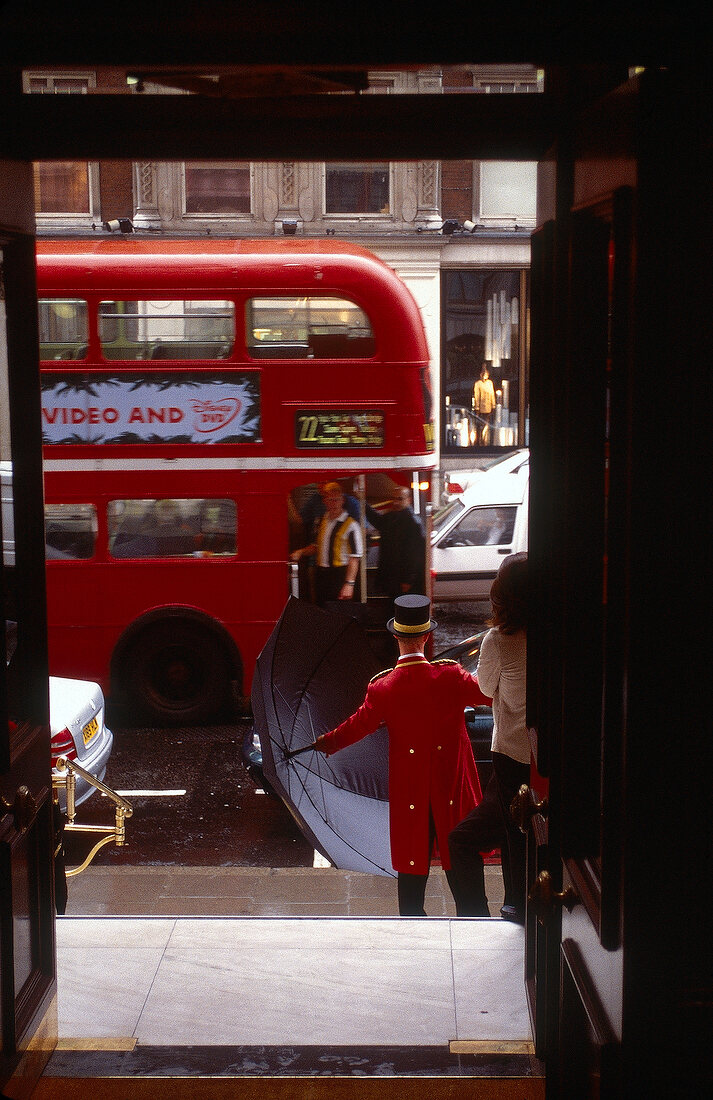 Ein roter Doppeldeckerbus und ein Portier mit Schirm im Vordergrund