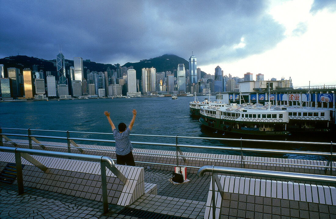 View of skyscrapers and moored ship at harbour with man in foreground, Hong Kong, China