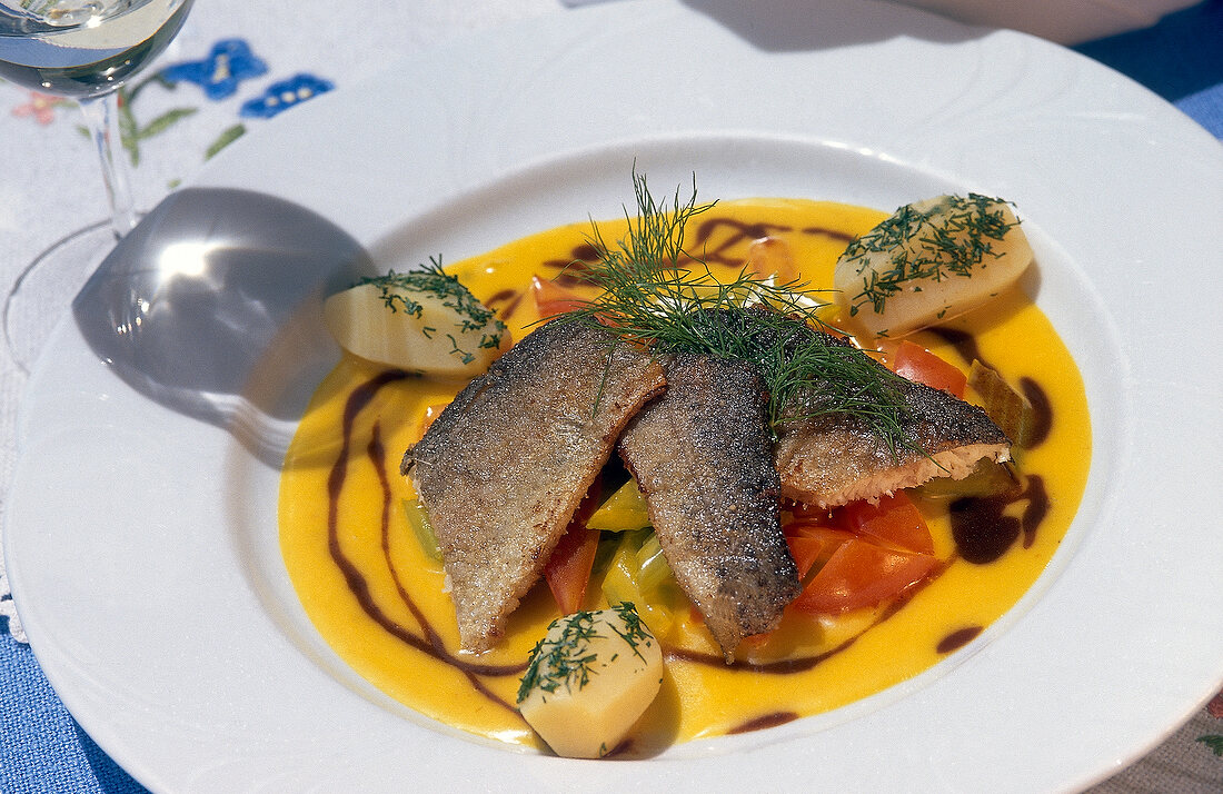 Brook trout fillet with saffron sauce and vegetables on plate