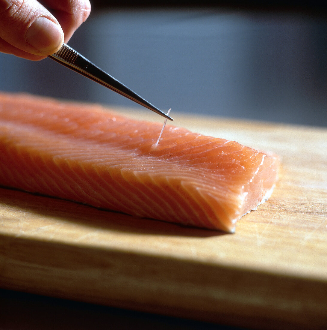 Close-up of raw salmon fillet being deboned on wooden board