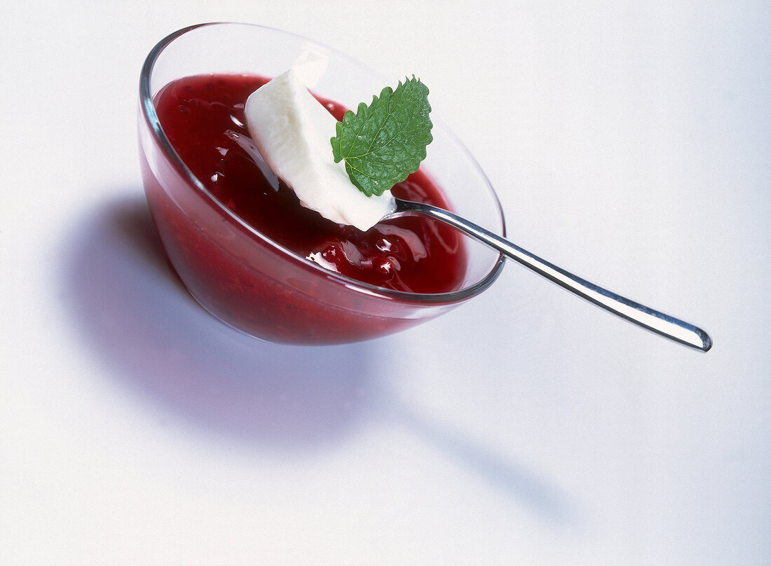 Red fruit jelly with yogurt and lemon balm leaf in bowl on white background