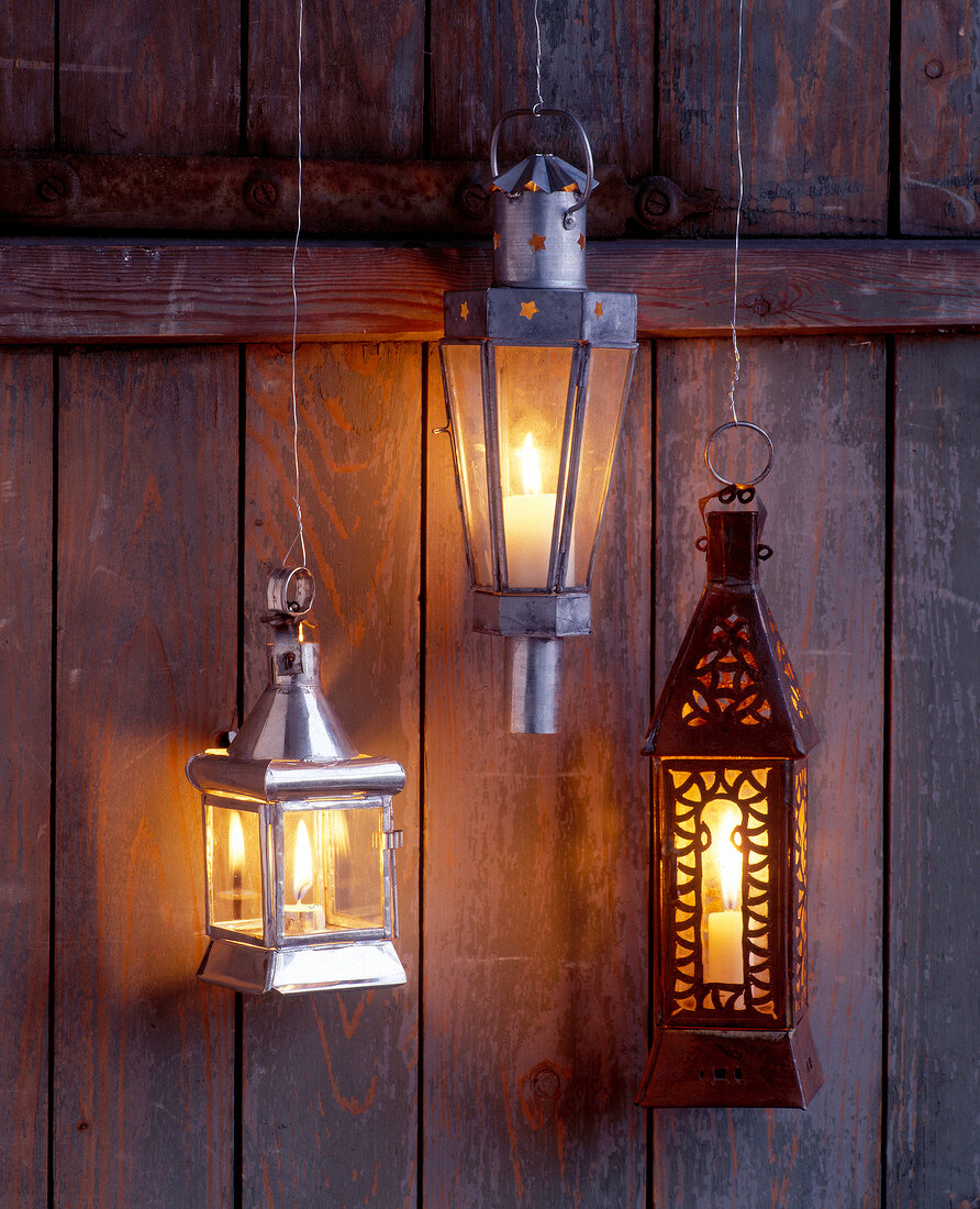 Three stable lanterns with flickering lit candles hanging on wires