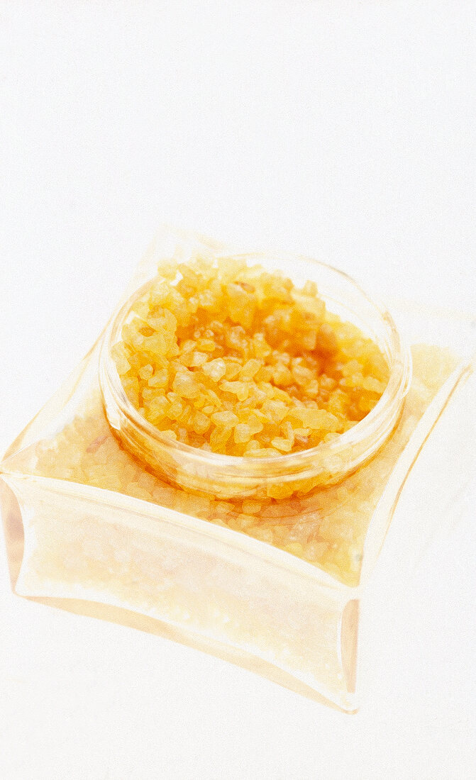 Yellow bath crystals in glass jar on white background