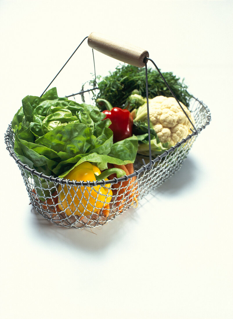 Variety of fresh vegetables in wire basket on white background