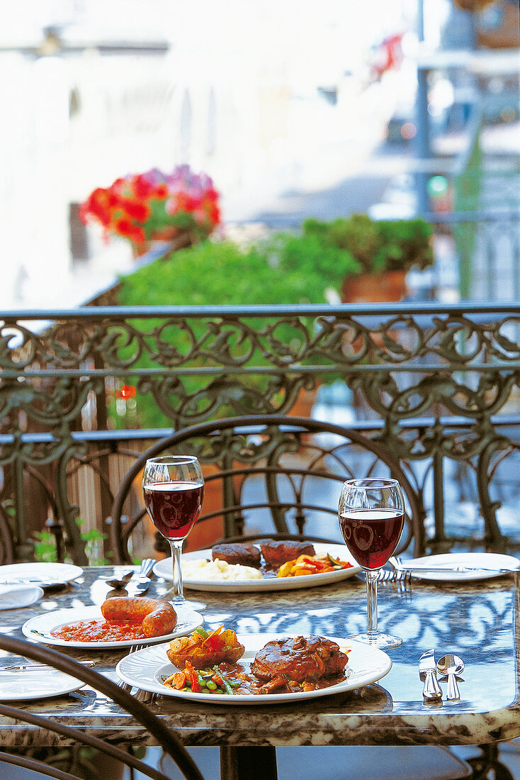 Pork with vegetables and sausage on plate and two glasses of red wine