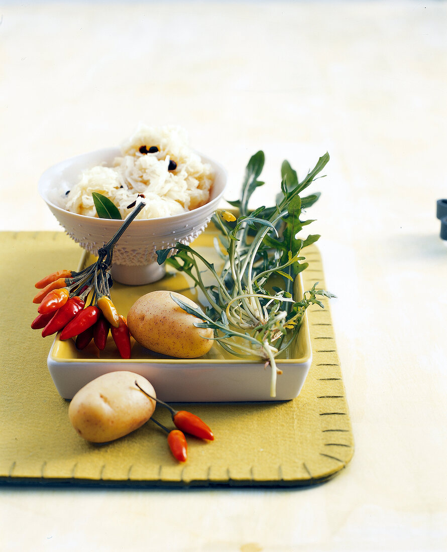 Two potatoes, arugula, chilli peppers with bowl on tray