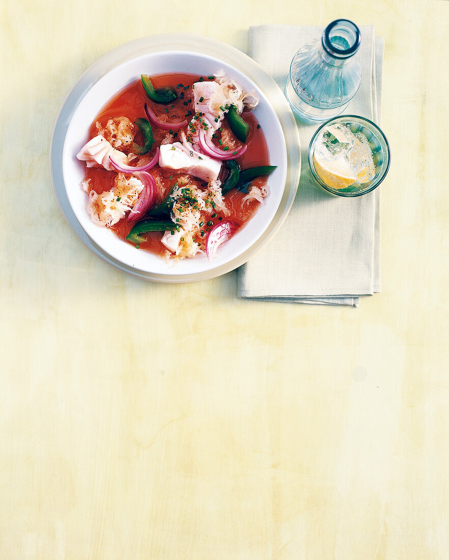 Fish soup with sauerkraut, onions and peppers in bowl with a glass of water, overhead view