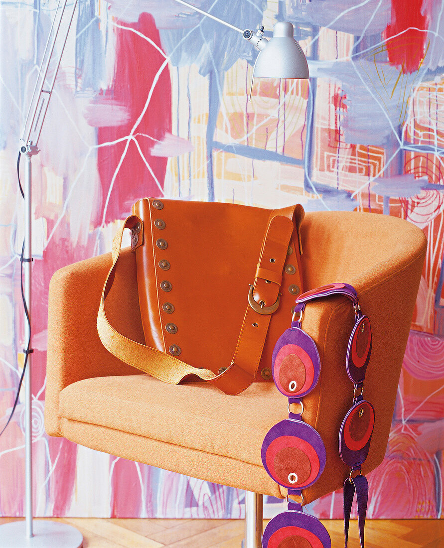 Brown leather bag with studs on orange chair with colourful wallpaper in background