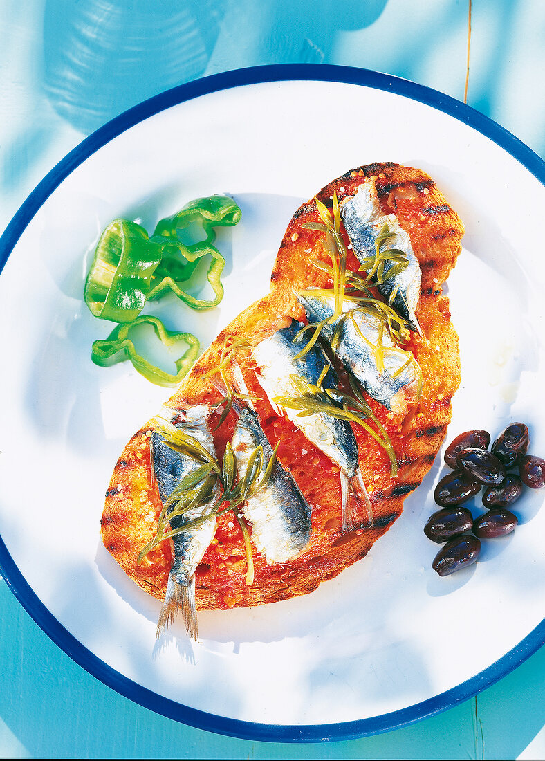 Sardines, toasted white bread with black olives and algae on plate, overhead view