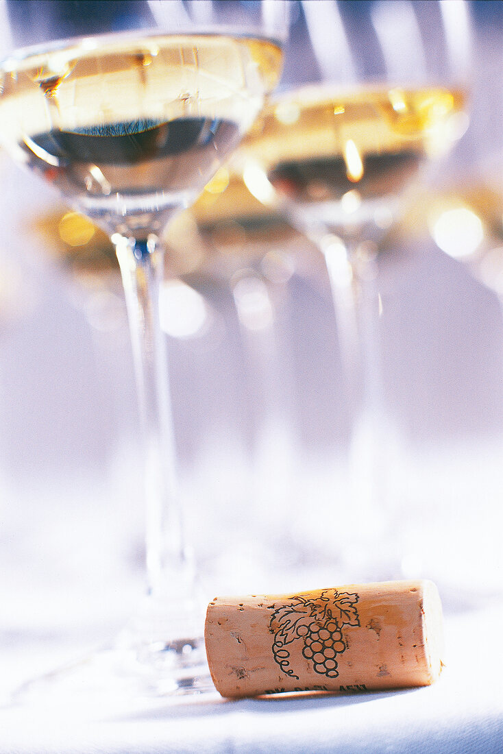 Close-up of white wine glasses with a wine cork