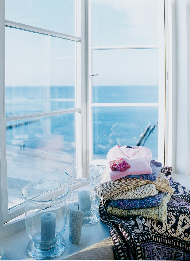 Stacked woollen sweaters with two candles on window sill