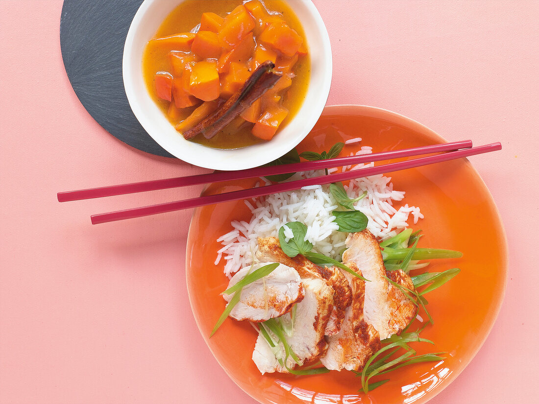 Huhn mit Kürbis-Zimt-Chutney, Reis, Stäbchen auf orangem Teller