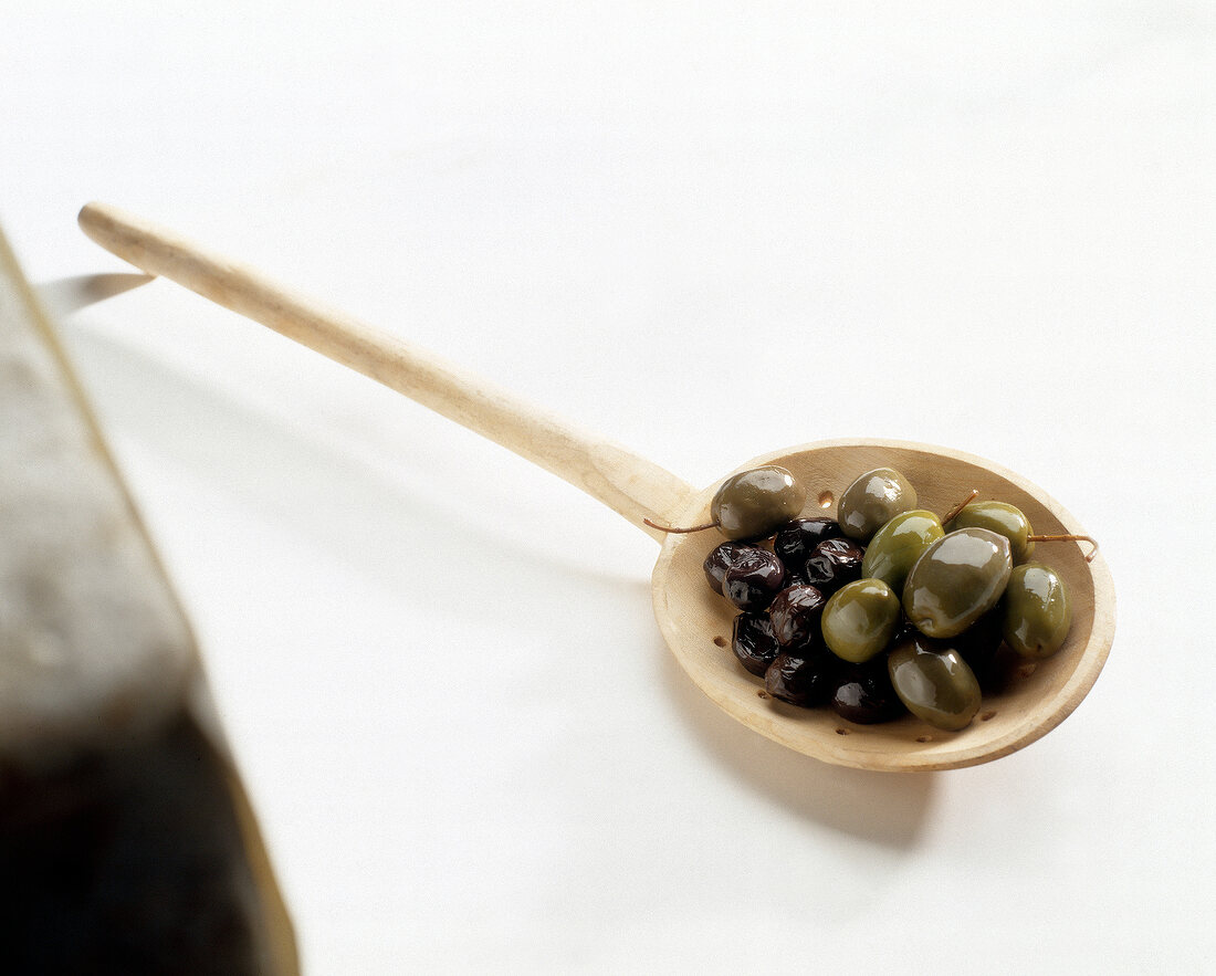 Green and black olives on large wooden spoon