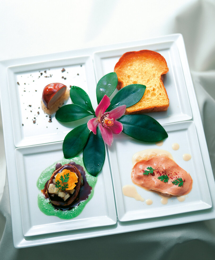 Foie grass variations on four square plates garnished with pink flower