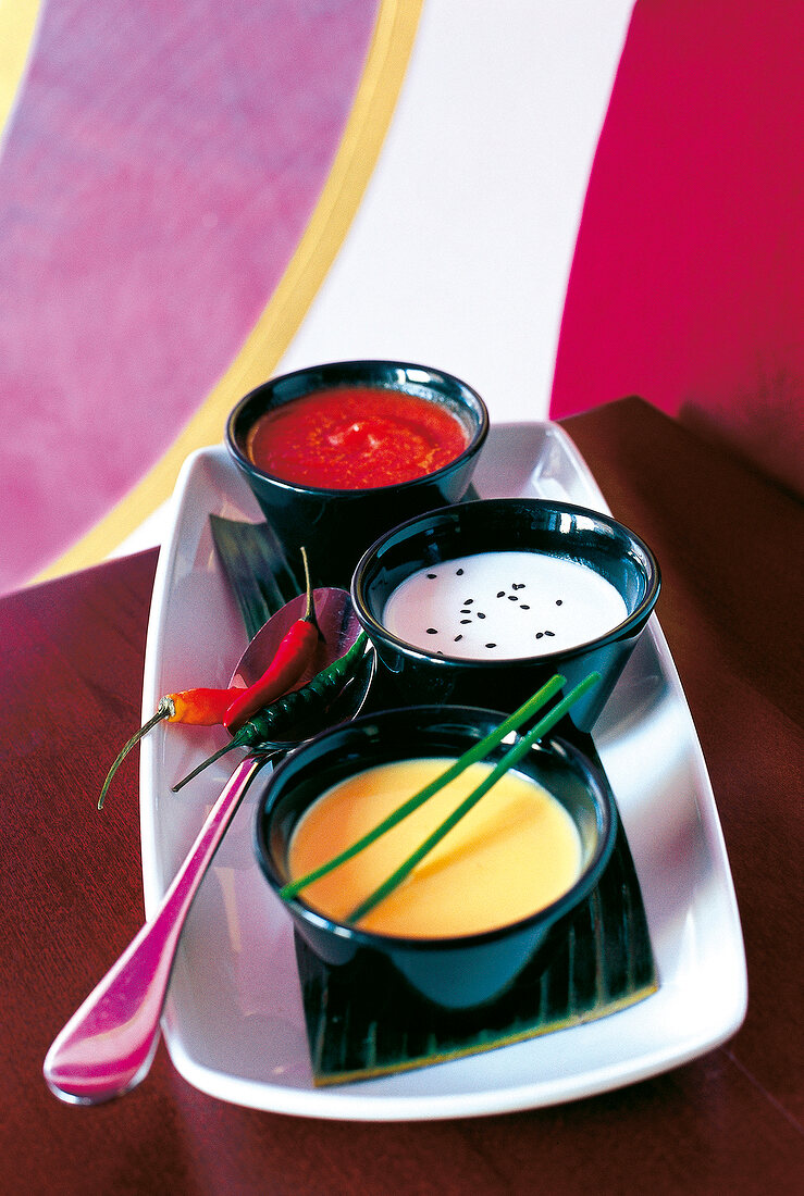 Colourful vegetable soup in three black bowls on tray with spoon