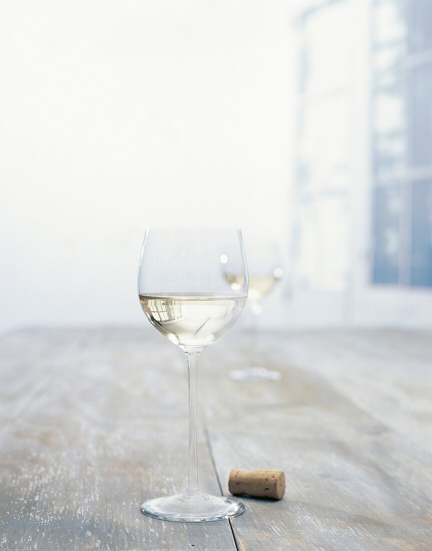 Glass of white wine and a cork on wooden table
