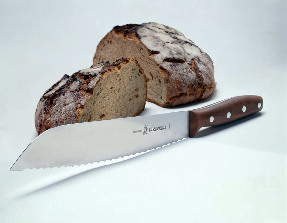 Bread knife placed in front halved brown bread on white surface