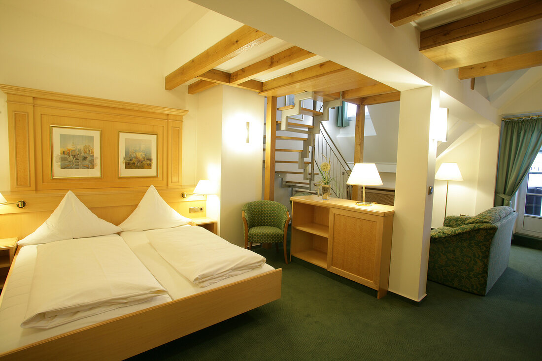 Bedroom with bed, cushion, chairs, table and stairs in hotel, Germany