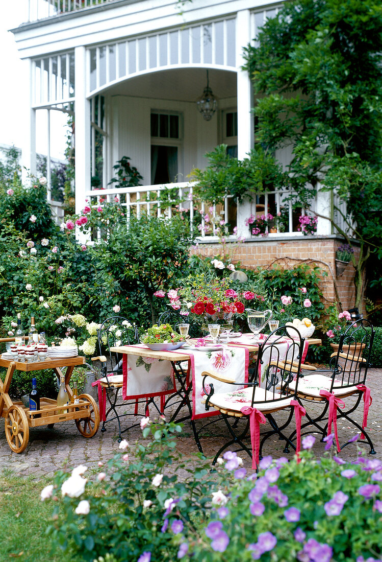 Metal table with chairs, table cloth, flower vase and food trolley in garden terrace