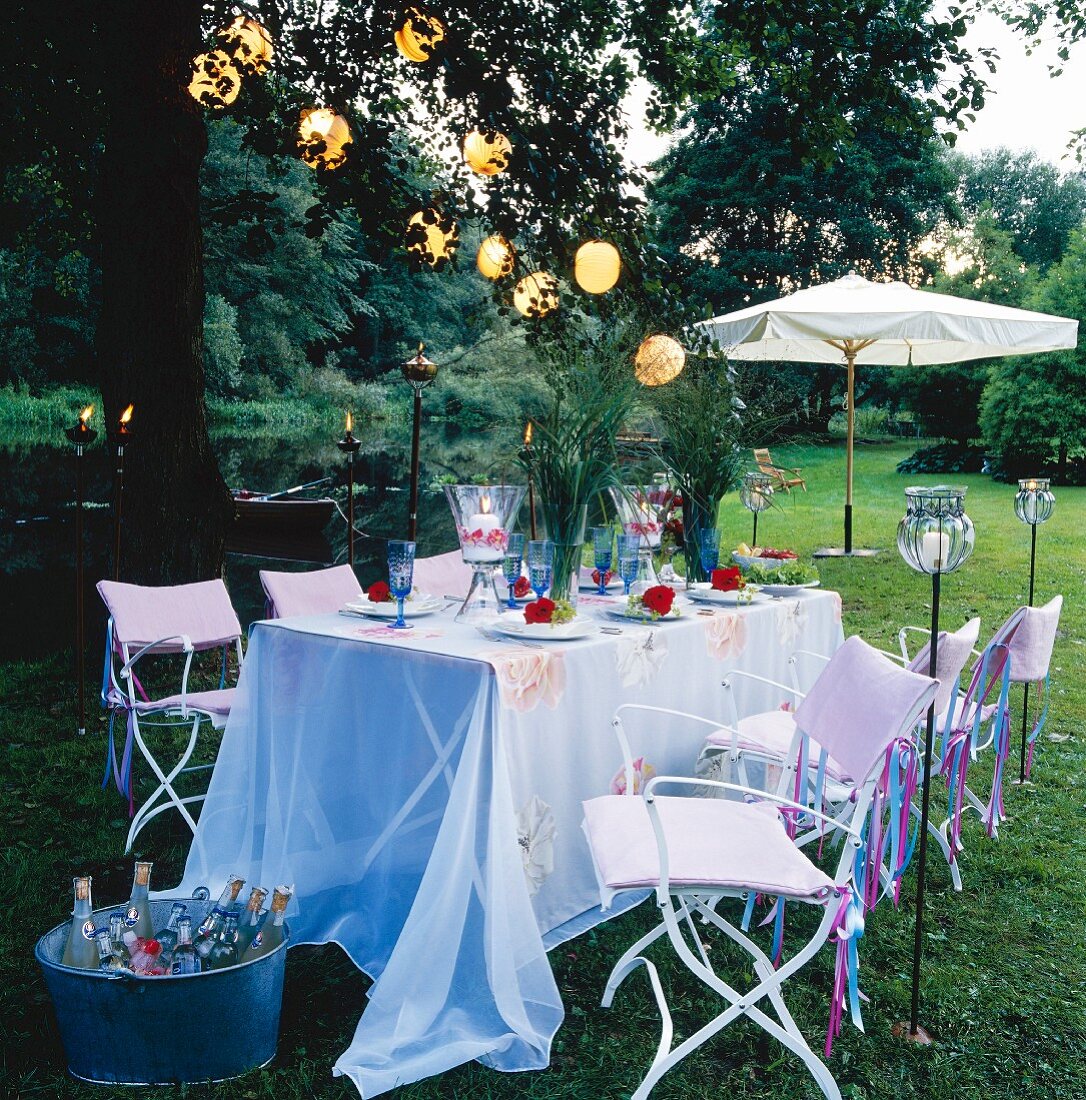 A festively laid table in a garden decorated with flowers, lanterns, lantern garlands and torches