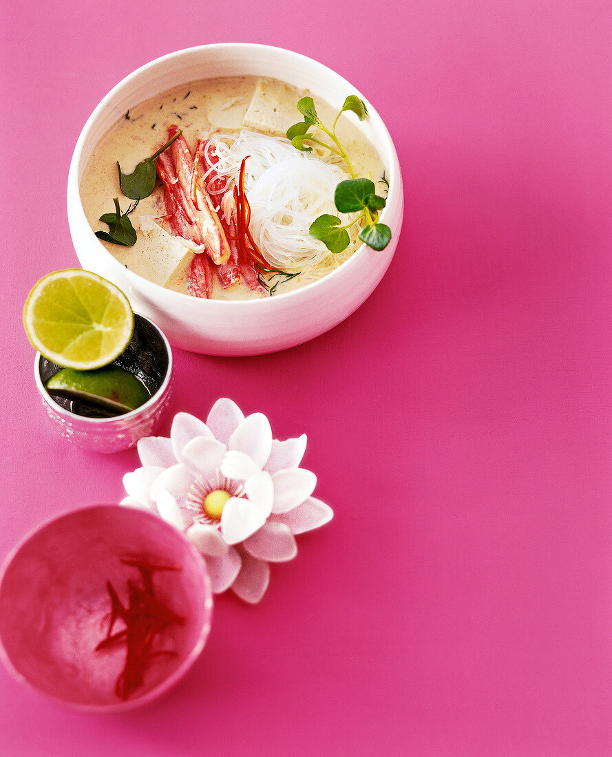 Singapore noodle curry in bowl served with two halved limes on pink background, copy space
