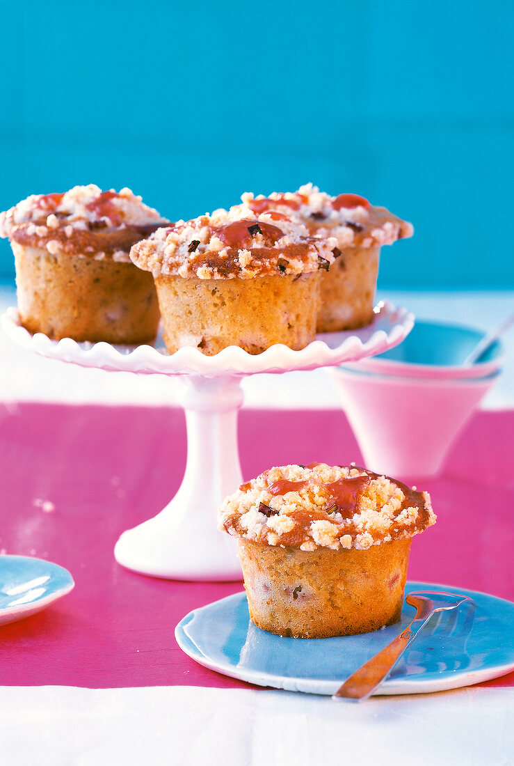 3 Rhabarber-Mandel-Muffins auf einer Servierplatte, 1 auf dem Teller