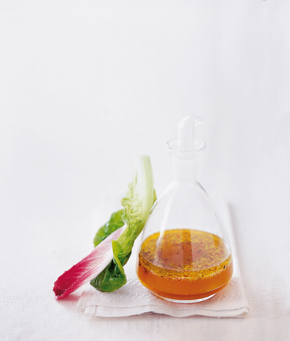 Eine Glasflasche mit Vinaigrette auf einem weißen Tuch und ein Salatblatt