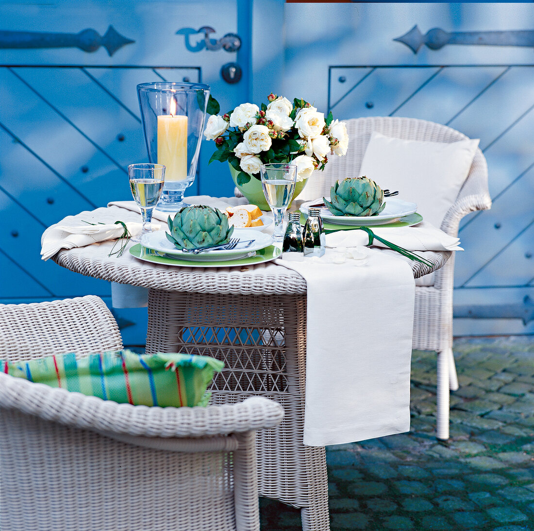 Wicker dining table with chair decorated with flowerpot, candles on garden terrace