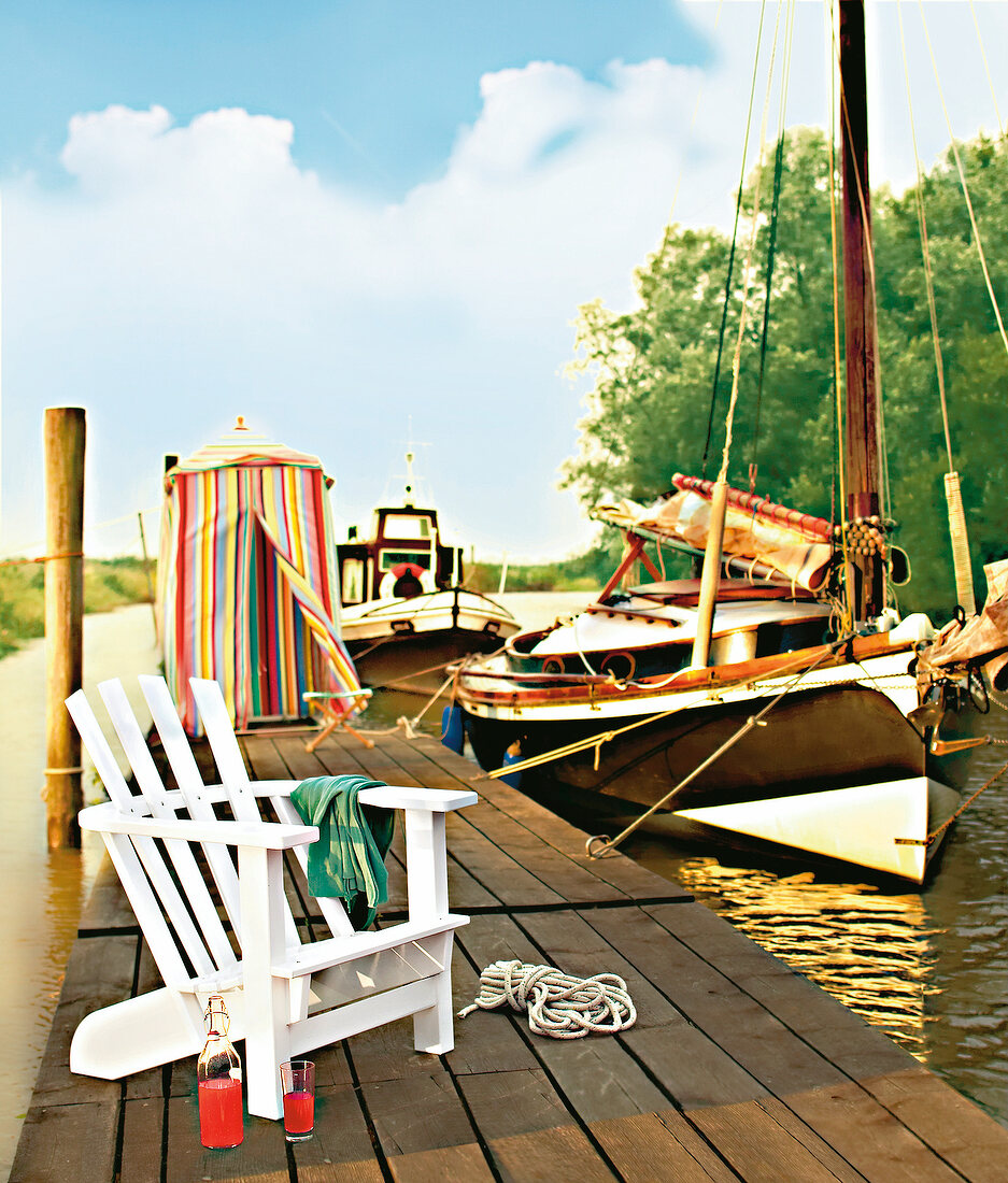 Bootssteg mit weißem Gartenstuhl Strandkabine und Booten