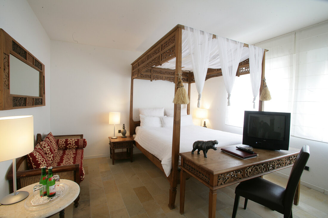 Bedroom with poster bed, chair, table, TV and sofa in hotel, Germany