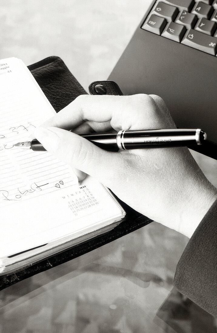 Close-up of woman writing with pen in a scheduler, black and white