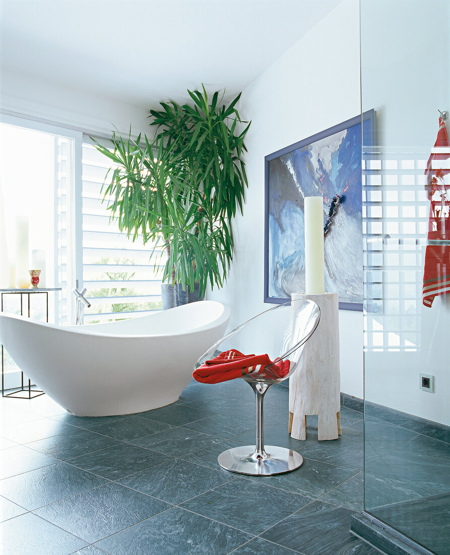 Oval bathtub and chair with painting on wall in bathroom