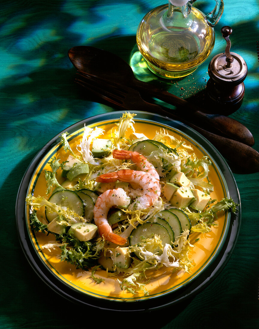 Salad with cucumber, avocado, frisee leaves and shrimp on plate