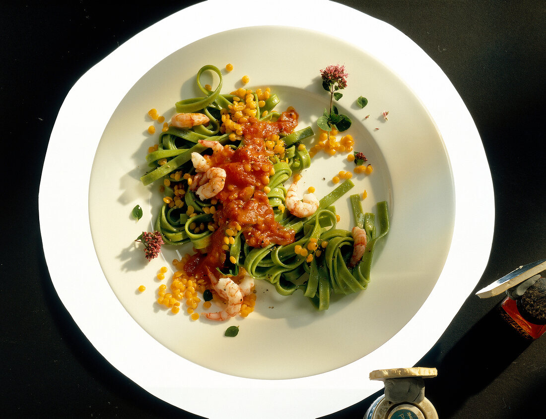 Green tagliatelle with lentils, tomato sauce and shrimp on plate