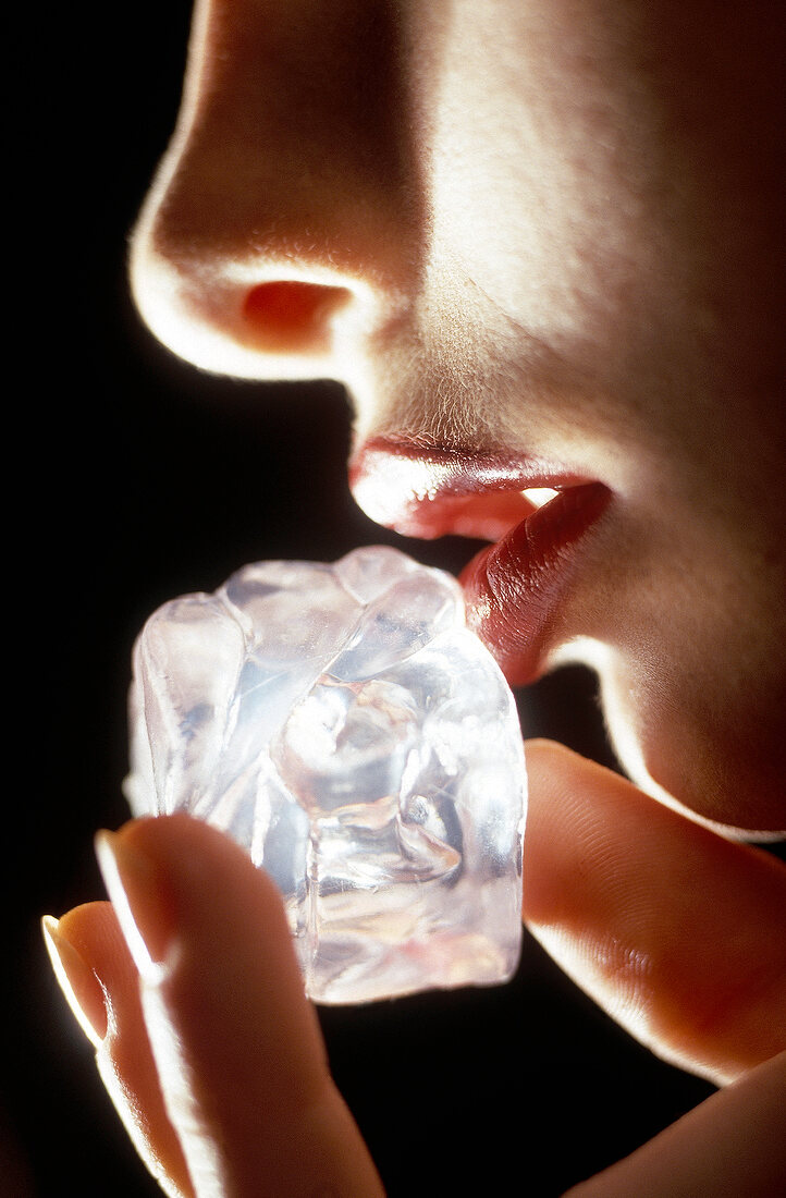 Frau bestreicht ihre geschminkten Lippen mit einem Eiswürfel