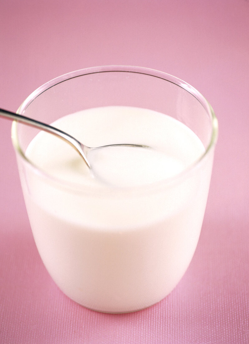Yogurt in jar with spoon on pink background
