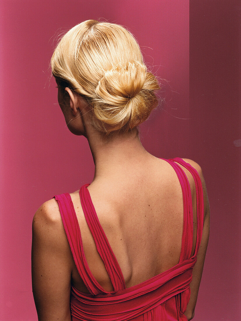Blonde Frau von hinten mit Knoten im Nacken, roter Hintergrund.